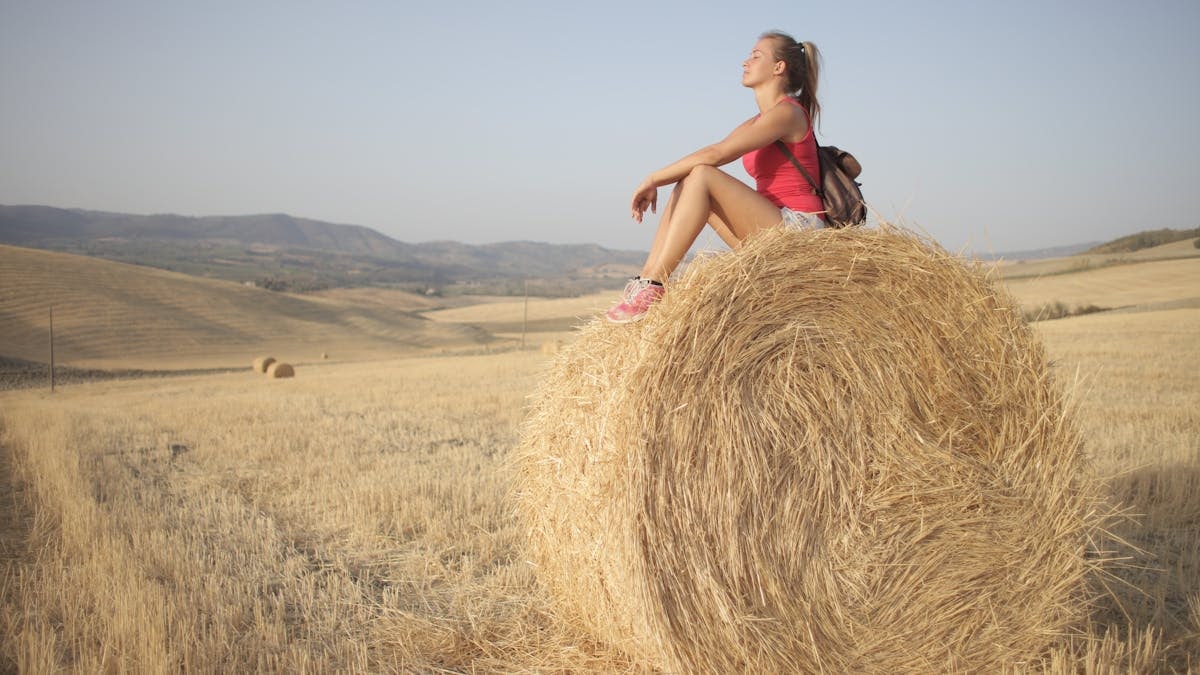 A young woman enjoying a peaceful moment on a hay bale in a sunny countryside field.